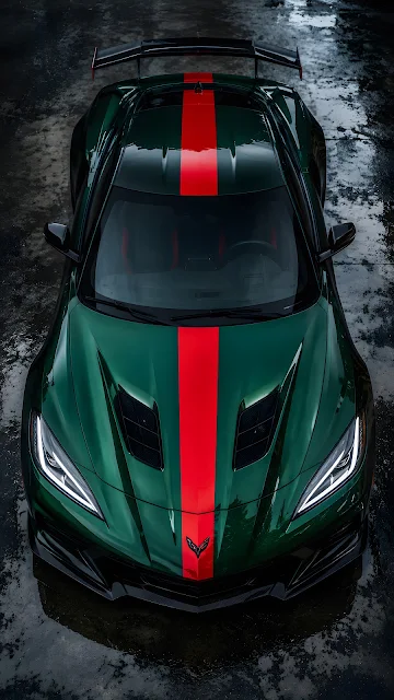 An overhead high-angle shot of a sleek forest green sports car with a wide red racing stripe parked on a wet asphalt surface.
