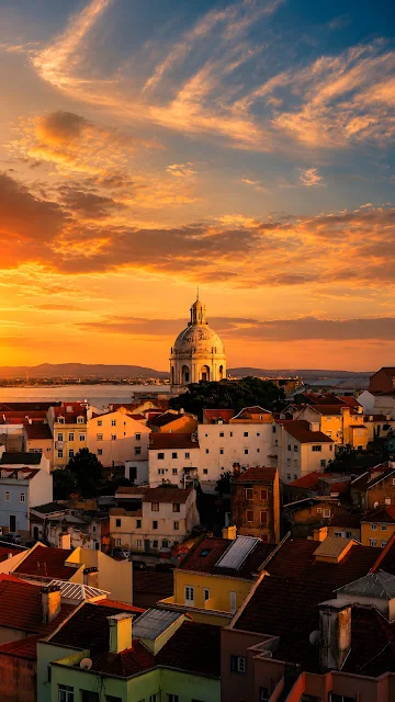 Historic domed building rises above dense terracotta rooftops beneath a glowing orange and blue evening sky.