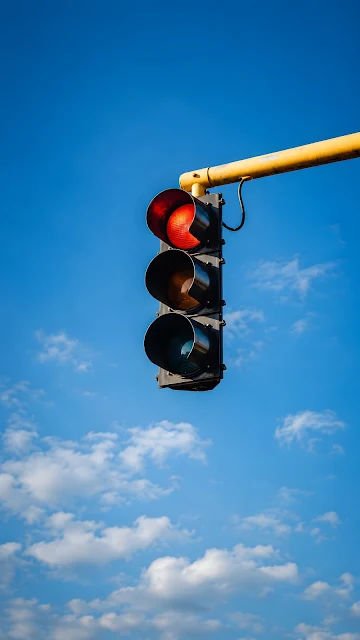 Low angle photograph of a modern vertical traffic signal with its red light glowing brightly against a vivid blue sky.