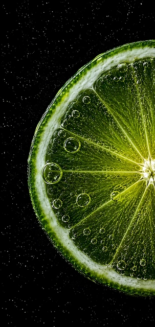 Close-up of a backlit green lime slice surrounded by sparkling bubbles on black.