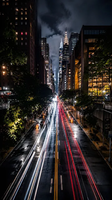 Long exposure night photo looking down a city avenue framed by tall skyscrapers with red and white light trails.