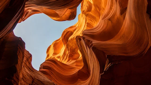 Warmly lit orange sandstone formations frame a small opening of light gray sky from below.