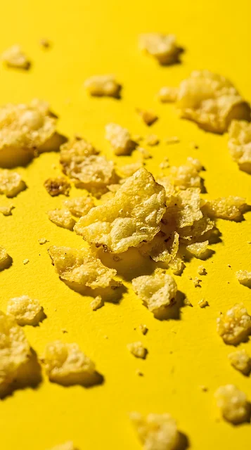Macro view of broken potato chips and crumbs on a yellow surface - Free mobile Wallpaper