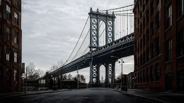 The steel structure of the Manhattan Bridge is perfectly framed between two tall red-brick buildings in Brooklyn.
