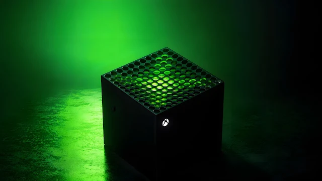 Matte black cube device with top circular mesh grille emitting bright green light onto a textured surface.