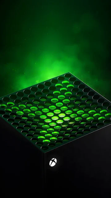 Close-up perspective of a matte black cuboid video game console featuring green LED lighting beneath its top ventilation grill.