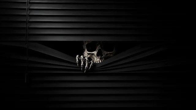Dramatic low-key photo of a human skull and bony fingers peeking between black horizontal blinds.