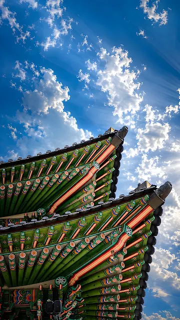 Detailed low angle view of intricately painted green wooden roof eaves against brilliant blue sky with sunburst.