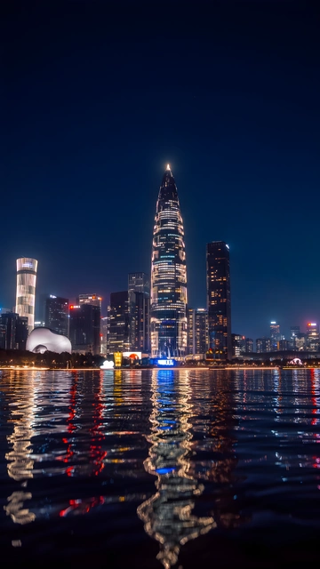 Shenzhen skyline and illuminated bamboo shoot tower reflecting across water at night.