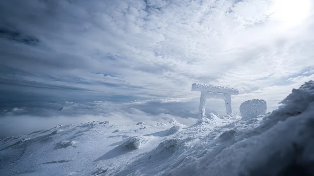 Wide shot of a snow-encrusted traditional wooden gate on a frozen mountain summit above a sea of clouds under bright sunlight.