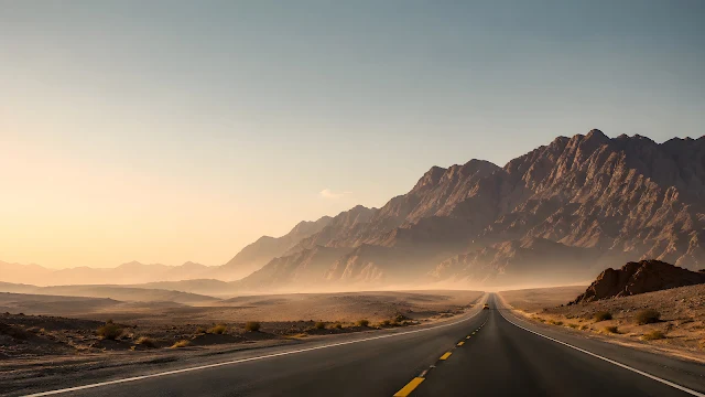 An endless asphalt road stretches symmetrically into a dusty desert horizon under distant mountains.
