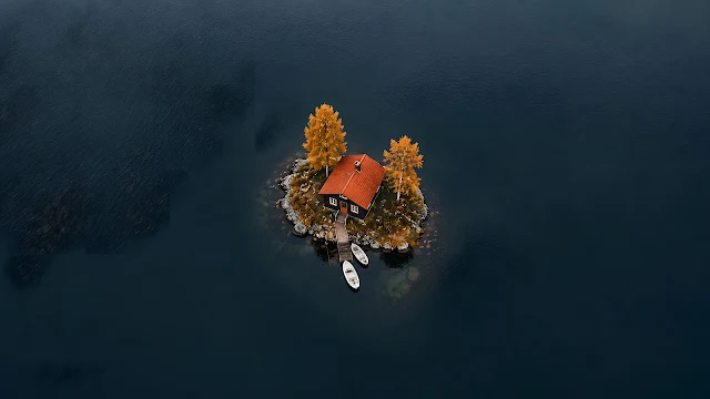 Top-down aerial photograph of a tiny dark house with a bright orange roof on a small island dock in deep water.
