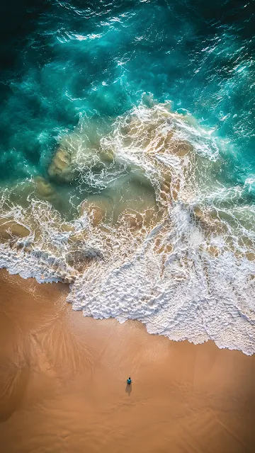 Aerial top-down view of turquoise sea water with white foam waves breaking along a clean golden sand shoreline.